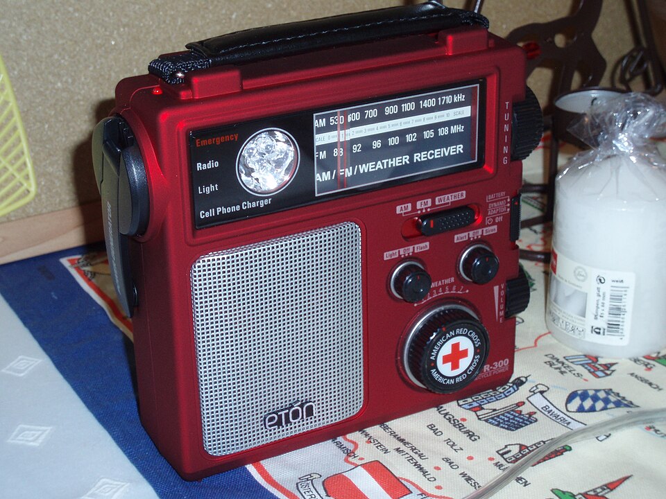 A red Eton emergency radio with a tuning dial, speaker grille and hand crank, for storm prep in Hiawatha, IA